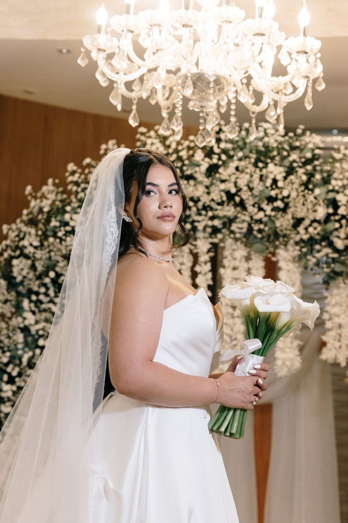 Noiva Nathalia com vestido brilhante, coque alto e buquê com flores brancas e roxas