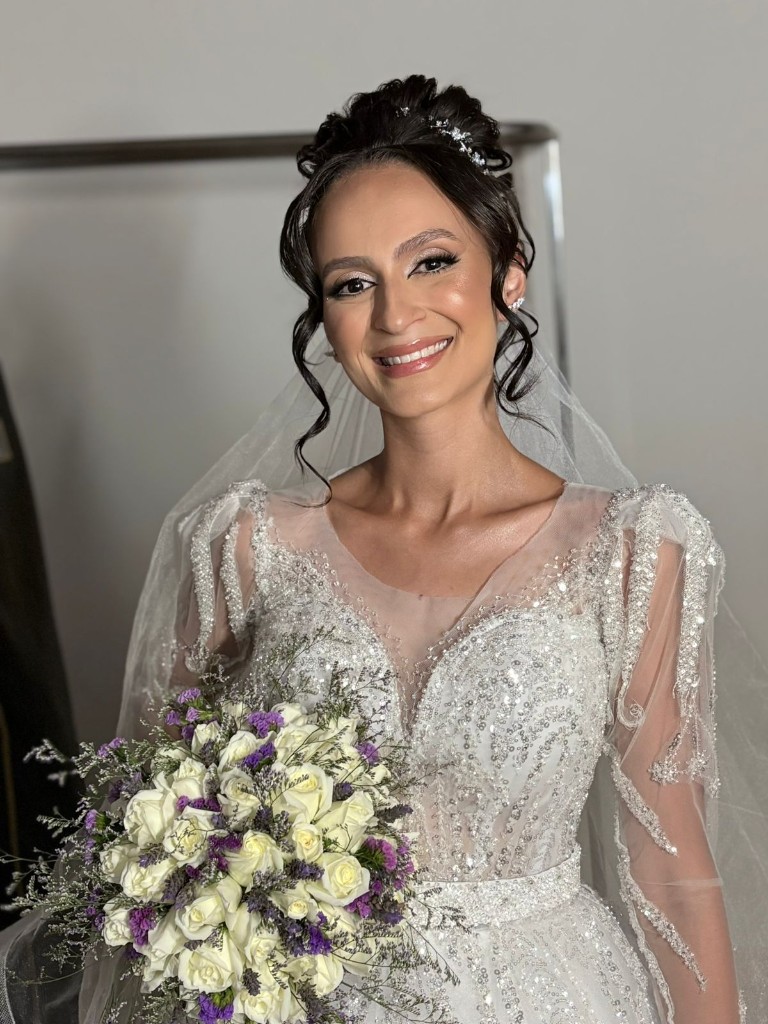 Noiva Larissa com coque alto, tiara delicada e maquiagem iluminada segurando buquê