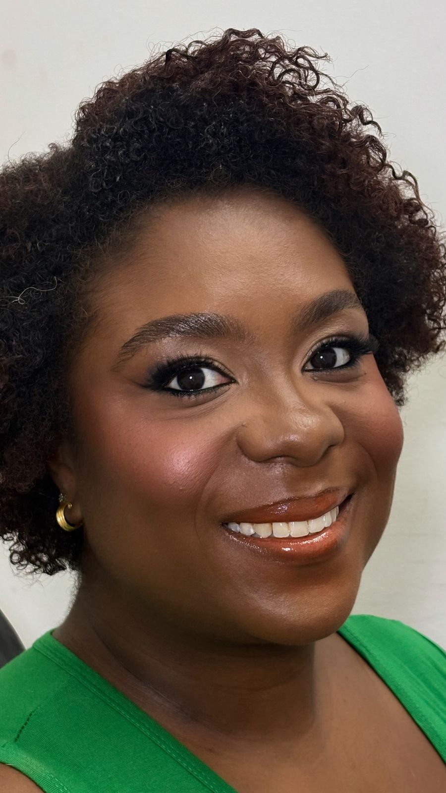 Retrato beauty com cabelo cacheado curto, pele radiante e maquiagem em tons quentes com sorriso.